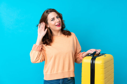 Traveler woman with suitcase over isolated blue background listening something