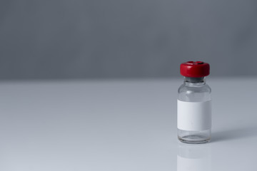 small bottle with a red cap of various medicines on a white, gray background. Antibiotics, vaccines or other injectable drugs.
