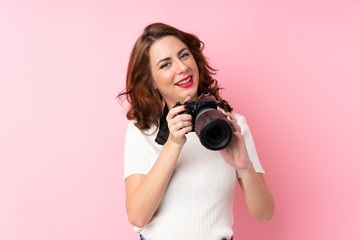 Young Russian woman over isolated pink background with a professional camera