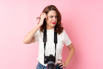 Young Russian woman over isolated pink background with a professional camera and thinking