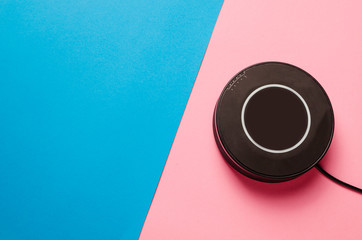 Black wireless charger on blue-pink paper background. Top view of the place for the text.