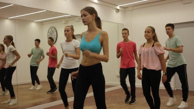 Group of teenagers participating in dance class, following their young female teacher in dance school