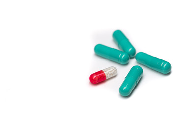 A few green pills and one red and white capsule on a white table.
