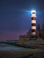 Majestyc lighthouse with beacon of light next to sea at night time full of stars.  © Viesturs