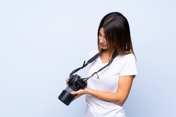 Young woman over isolated blue background with a professional camera