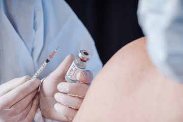 Glass medical bottle in a doctor's hand. A bottle with a vaccine holds a hand in silicone gloves in a policlinic.  The doctor gives the vaccine. A breakthrough in treatment. Antiviral vaccination.