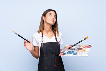 Young woman over isolated blue background holding a palette and thinking an idea