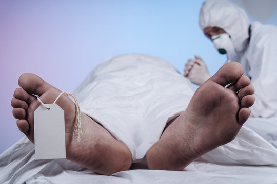 Feet of a dead body, with an identification tag - blank sign attached to a big toe. Coronavirus victim. Doctor depressed after the death of another patient.