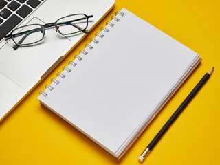 Workplace - laptop, notebook, glasses and pencil for remote work on a yellow background table. Freelance desktop for home or office. Background with copy space.