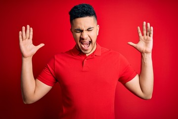 Young handsome man wearing red casual polo standing over isolated background celebrating mad and crazy for success with arms raised and closed eyes screaming excited. Winner concept