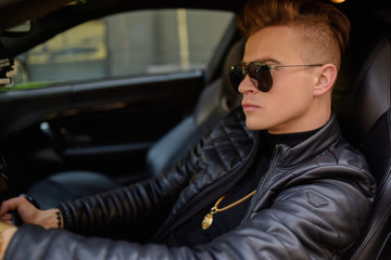 A businessman is sitting in a golden car. A man is driving inside a car. Driver. Chic man with glasses, with a perfect haircut, glasses, fashionable. Freelancer. Rich boy. A teenager drives a car.