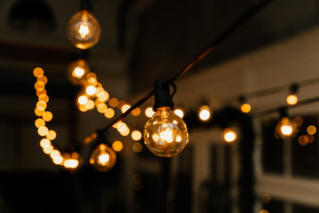 Luminous incandescent lamps hang in the form of a garland on wires, against the background of a shop window. Background from a garland. Incandescent lamps.