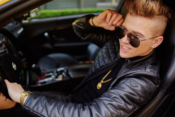 Fototapeta na wymiar A businessman is sitting in a golden car. A man is driving inside a car. Driver. Chic man with glasses, with a perfect haircut, glasses, fashionable. Freelancer. Rich boy. A teenager drives a car.