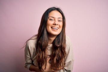 Fototapeta premium Young beautiful brunette woman wearing casual sweater standing over pink background smiling and laughing hard out loud because funny crazy joke with hands on body.