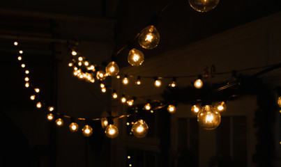 Luminous incandescent lamps hang in the form of a garland on wires, against the background of a shop window. Background from a garland. Incandescent lamps.