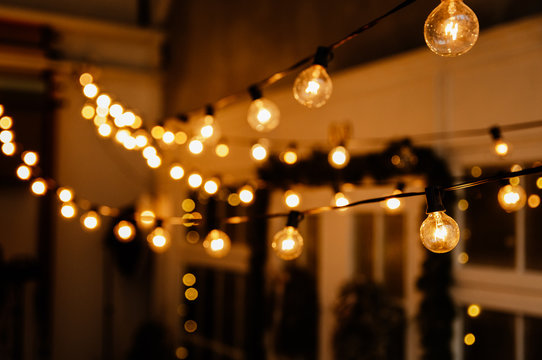 Luminous incandescent lamps hang in the form of a garland on wires, against the background of a shop window. Background from a garland. Incandescent lamps.