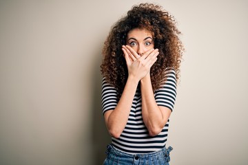 Young beautiful woman with curly hair and piercing wearing casual striped t-shirt shocked covering mouth with hands for mistake. Secret concept.