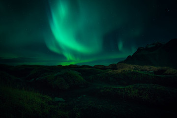 Fototapeta na wymiar Image of Northern Lights illuminating the sky with a mountain landscape backdrop in Iceland during night time 