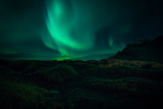 Image of Northern Lights illuminating the sky with a mountain landscape backdrop in Iceland during night time 