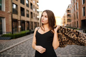 Fototapeta premium Gorgeous girl walks about the city. Brunette with long hair in a black dress and a leopard cape. Girl, fashion photo, street fashion. Fashionable girl walks in the city of Europe, travels.