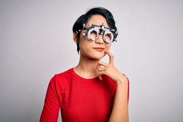 Young beautiful asian girl wearing optometry glasses standing over isolated white background with hand on chin thinking about question, pensive expression. Smiling with thoughtful face. Doubt concept.