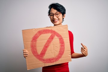 Young beautiful asian girl holding banner with prohibited signal over white background very happy...
