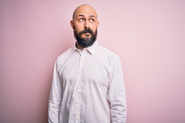 Handsome bald man with beard wearing elegant shirt over isolated pink background smiling looking to the side and staring away thinking.