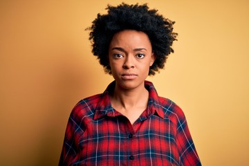 Obraz na płótnie Canvas Young beautiful African American afro woman with curly hair wearing casual shirt with serious expression on face. Simple and natural looking at the camera.
