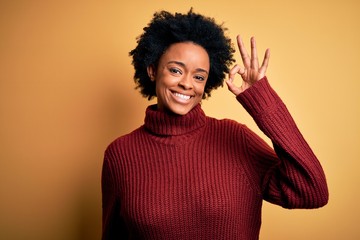 Fototapeta na wymiar Young beautiful African American afro woman with curly hair wearing casual turtleneck sweater smiling positive doing ok sign with hand and fingers. Successful expression.