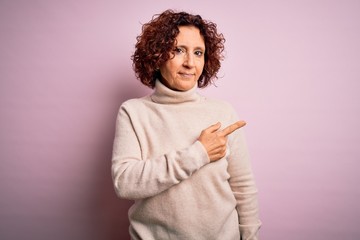 Middle age beautiful curly hair woman wearing casual turtleneck sweater over pink background Pointing with hand finger to the side showing advertisement, serious and calm face