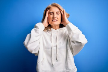 Middle age beautiful blonde sportswoman wearing sportswear over isolated blue background suffering from headache desperate and stressed because pain and migraine. Hands on head.