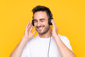 Young man over yellow background listening music and singing