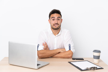 Young business man with a mobile phone in a workplace having doubts and with confuse face expression