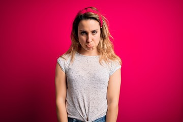 Young beautiful blonde woman wearing casual t-shirt standing over isolated pink background depressed and worry for distress, crying angry and afraid. Sad expression.