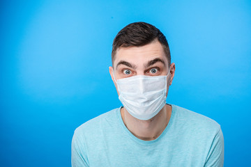 Portrait of handsome young european man wearing mask in studio. Isolated on blue background. Infection and quarantine concept