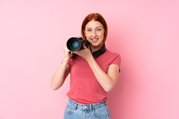 Young redhead woman over isolated pink background with a professional camera