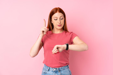 Young redhead woman over isolated pink background looking at the hand watch