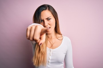 Young beautiful blonde woman with blue eyes wearing white t-shirt over pink background pointing displeased and frustrated to the camera, angry and furious with you