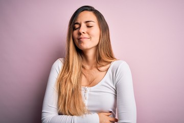 Naklejka premium Young beautiful blonde woman with blue eyes wearing white t-shirt over pink background with hand on stomach because indigestion, painful illness feeling unwell. Ache concept.