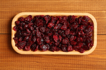 Dried cranberries lying on a bamboo plate on a wooden table. Closeup. Macro