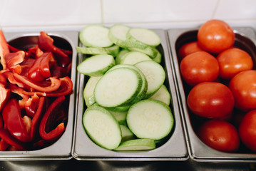 Variety of sliced vegetables prepped for cooking in a professional kitchen, such as bell pepper, zucchini, tomatoes