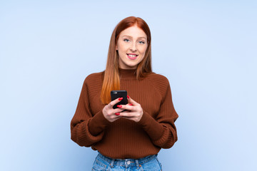 Young redhead woman over isolated blue background sending a message with the mobile