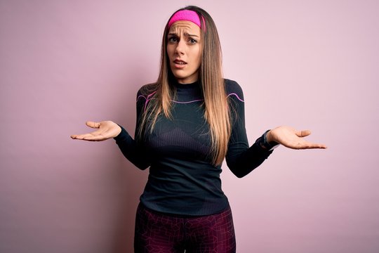 Young blonde fitness woman wearing sport workout clothes over isolated background clueless and confused with open arms, no idea concept.