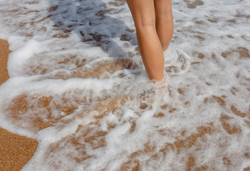 Woman legs walking on sandy beach with sea waves