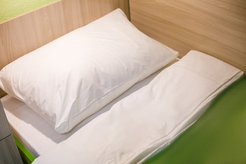 Fototapeta na wymiar A bed with a white pillow and a green blanket in the cabin of a cruise ship.