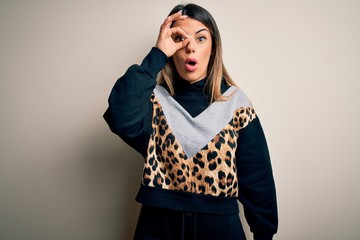 Young beautiful woman wearing casual sweatshirt standing over isolated white background doing ok gesture shocked with surprised face, eye looking through fingers. Unbelieving expression.