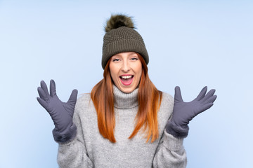 Young redhead Russian woman with winter hat over isolated blue background unhappy and frustrated with something