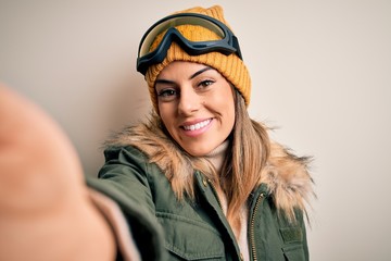 Young brunette skier woman wearing snow clothes and ski goggles make selfie by camera with a happy face standing and smiling with a confident smile showing teeth