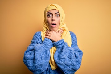 Young beautiful brunette muslim woman wearing arab hijab over isolated yellow background shouting suffocate because painful strangle. Health problem. Asphyxiate and suicide concept.