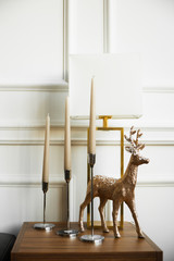 Three candles in candlesticks, a decorative golden deer on a bedside table - 333573965